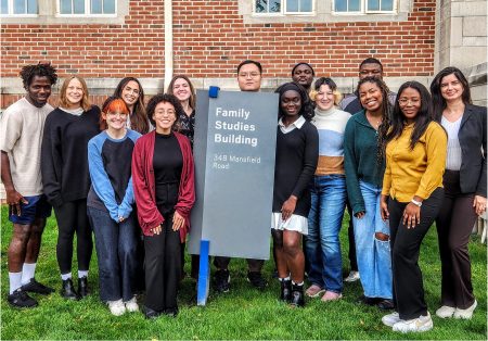 Cohort of 14 first year graduate students pose next to Family Studies Building sign